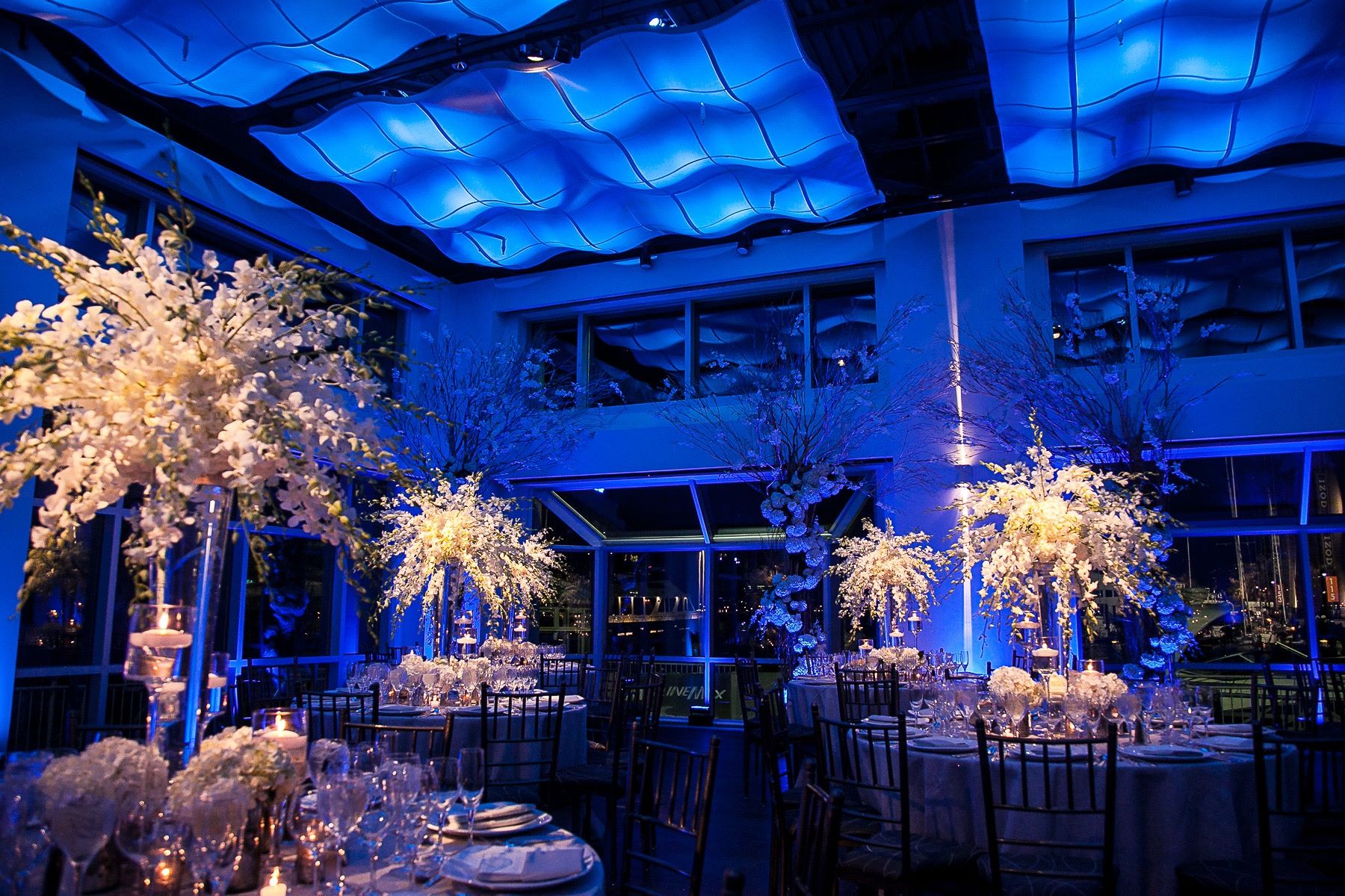 Current set with dining tables tall flower center pieces and blue lights over