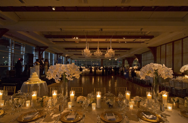 Pier Sixty set up with a dance floor and a mix of rectangular and round tables with candles, white flowers and a band on stage on the left.