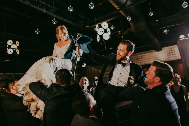 Newlyweds laughing as they crowdsurf in chairs