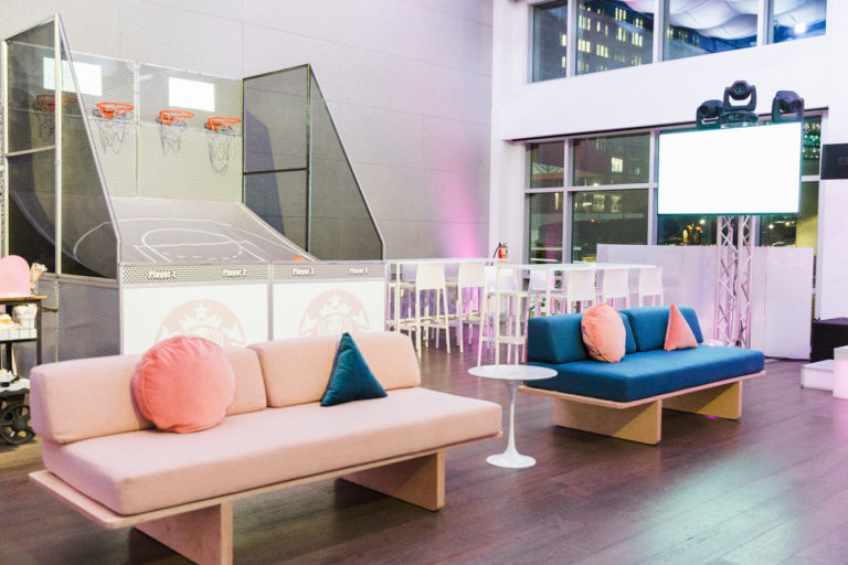 Pastel couches with geometric pillows in front of basketball game.