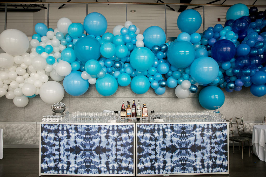 Tie-dyed bar counter in front of giant blue balloon decorative wall.