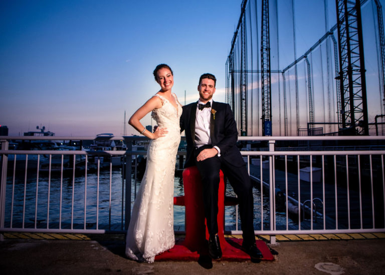 Bride and groom pose at railing along waterfront