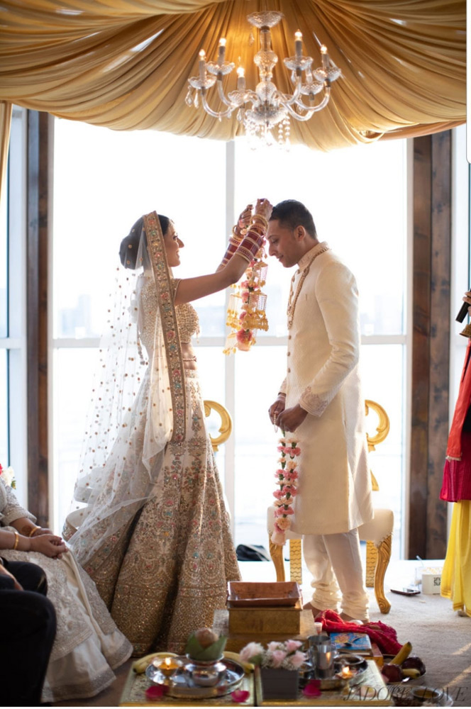 Bride placing floral necklace on groom in traditional Indian wedding