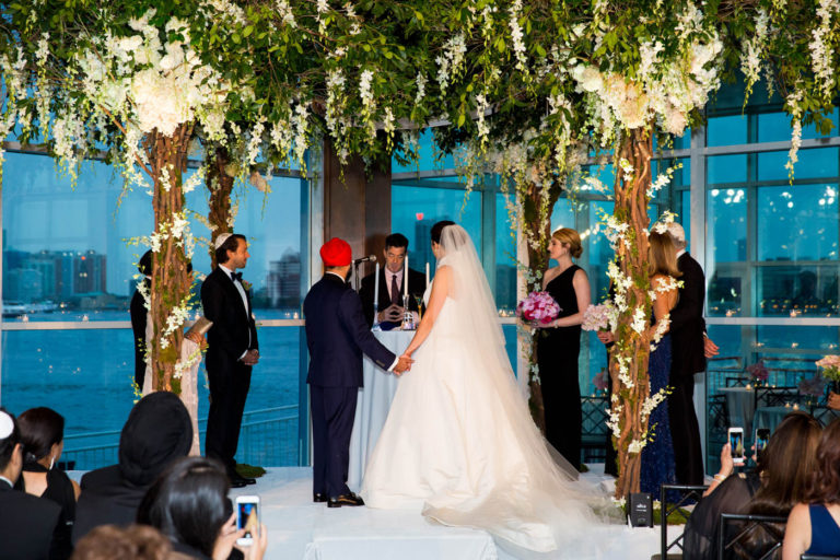 Officiant performing wedding ceremony under white flowers