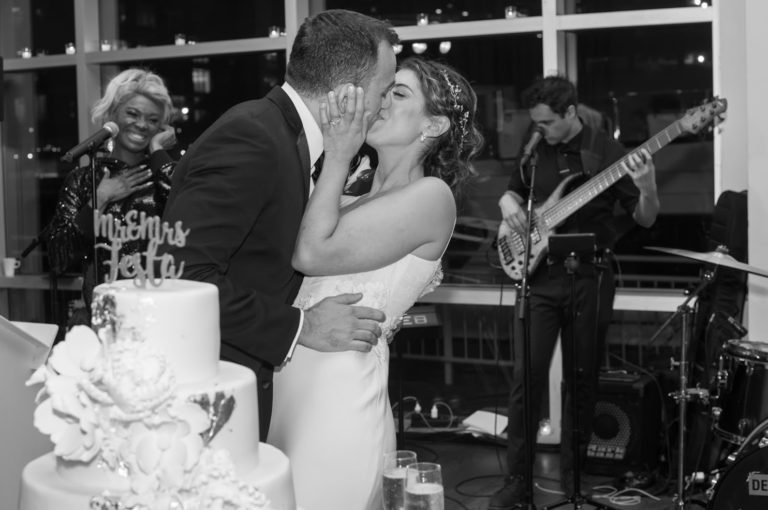 Bride and Groom by wedding cake kissing at Current