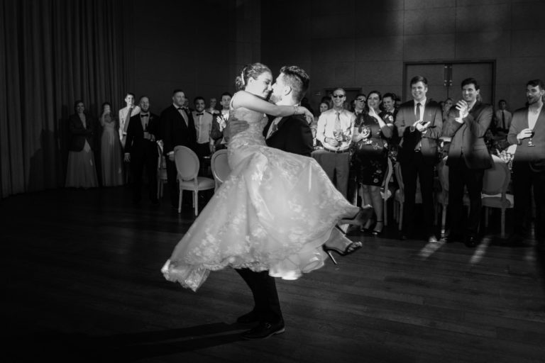Groom holding bride while dancing in the dance floor, guests are observing in the background
