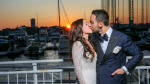 Bride and groom kissing, standing in the Current Veranda, with the sunset over the marina