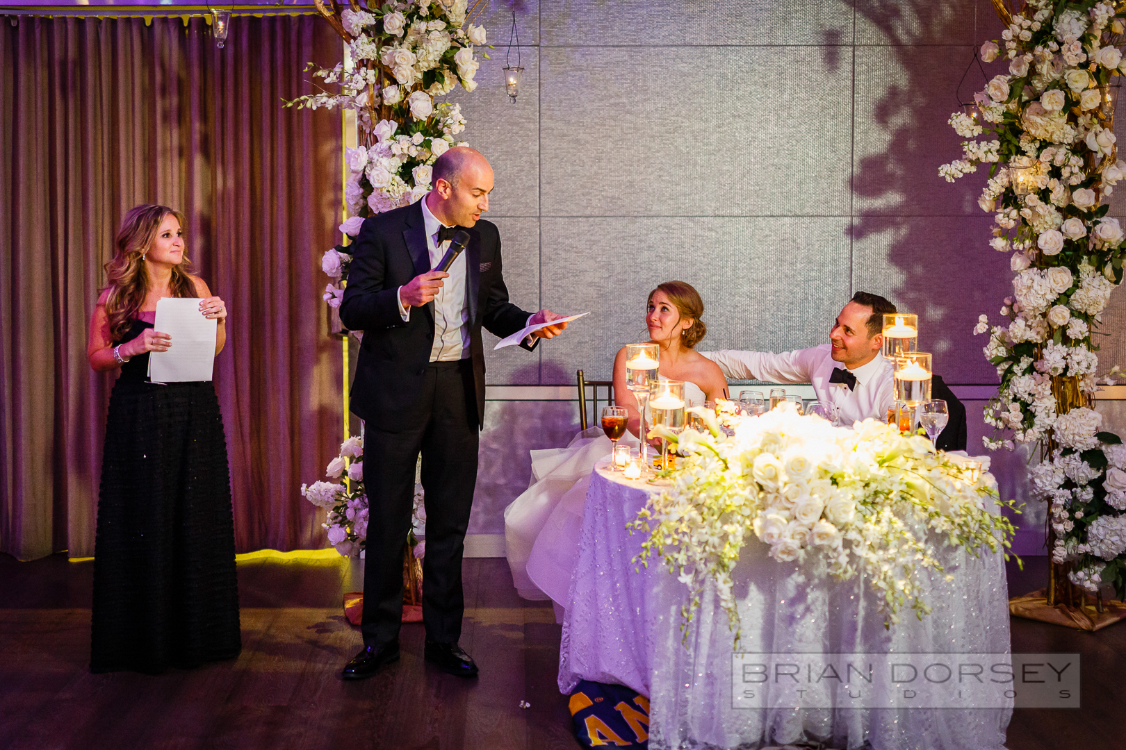 father of the bride is giving a speech to his left bride and groom are seated at their table