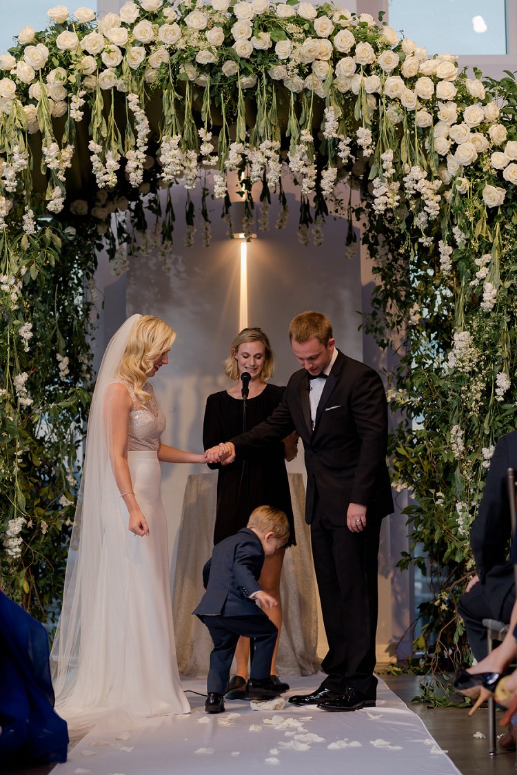 Bride, groom, minister and child under the flower arch during the ceremony at Current