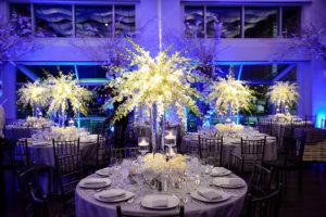 three dinner tables set with tall white center pieces at Current