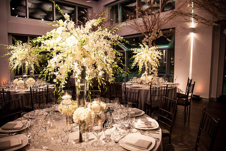 Dinner tables with white tall center pieces and amber lighting in the background