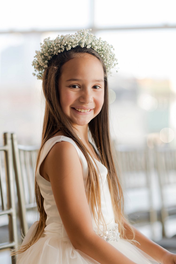 flower girl seated on a chair with a flower crown smiling for the picture