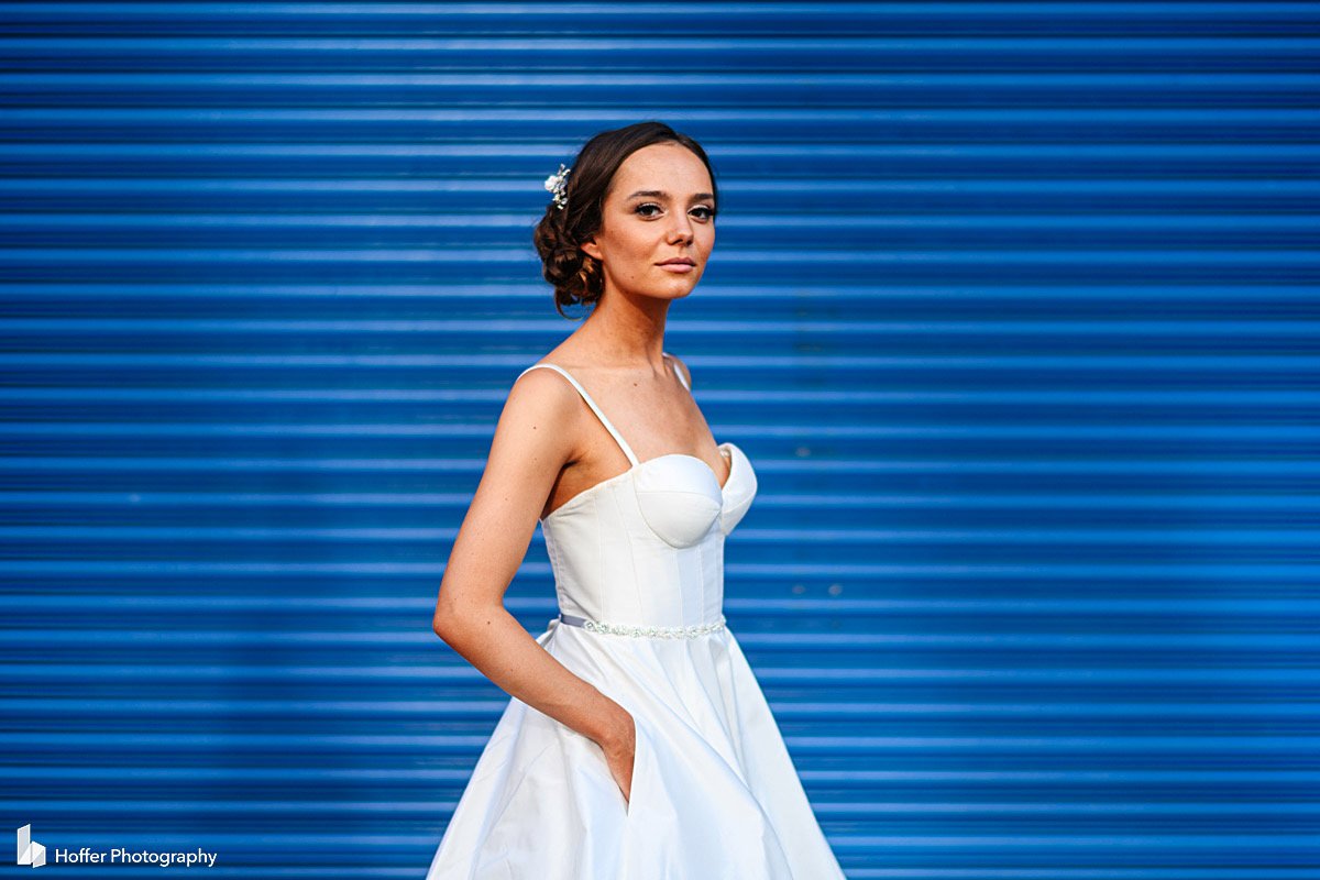 Bride with hands in her dress pockets, standing outside of Pier 59 in front of a blue garage door