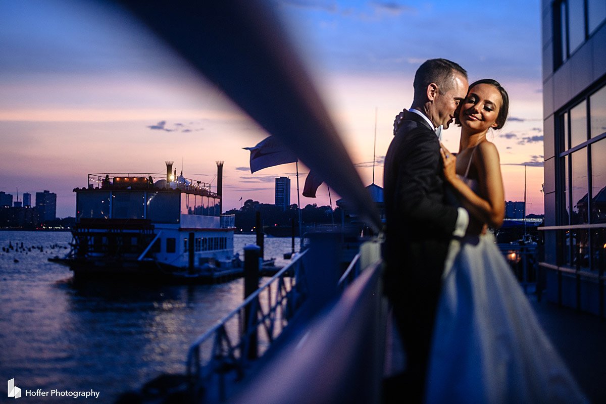 Sunset over the marina in purple and pink colors, bride and groom holding each other in the Current Veranda